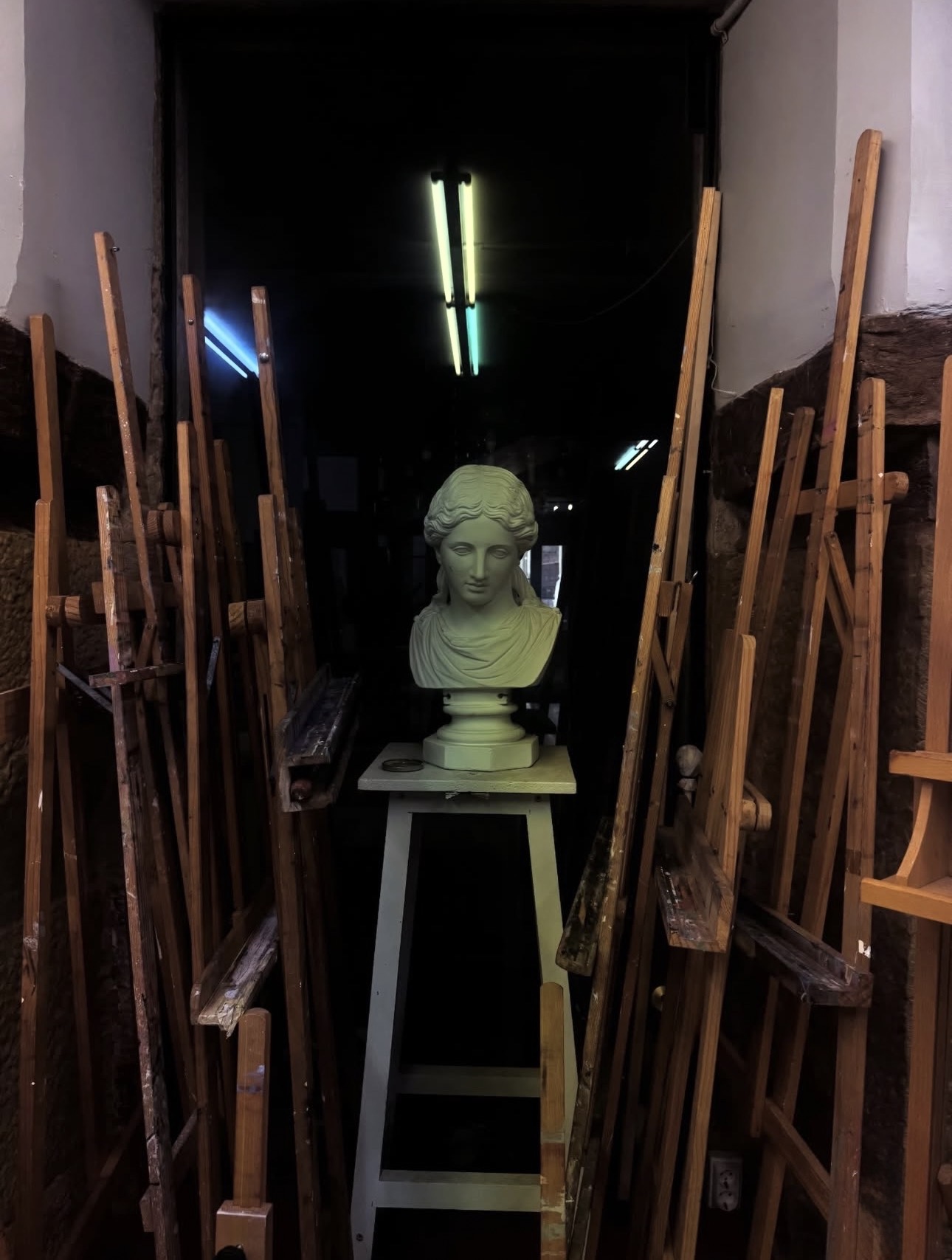 Caballetes de madera apilados en el pasillo del taller junto a un busto de escayola